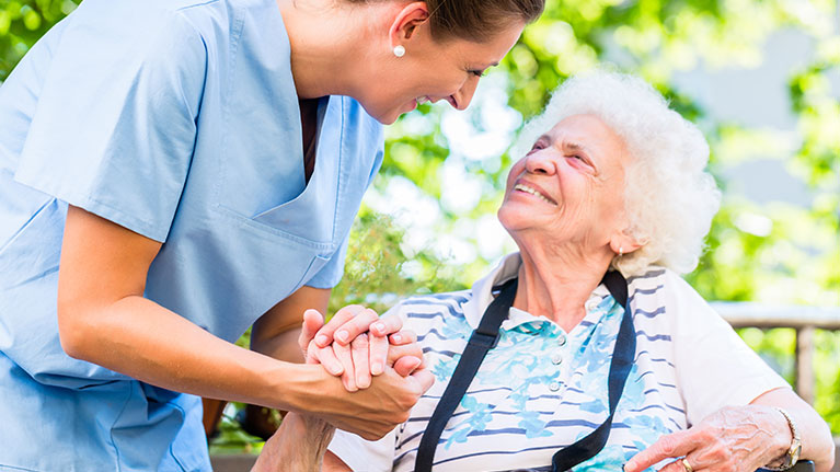Female nurse holding hands with smiling senior patient. 