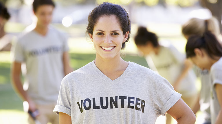 Young woman smiling, wearing a gray volunteer shirt.