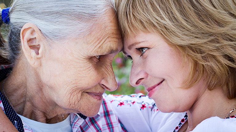 Older woman and younger woman with their forehead pressed together while looking at each other.