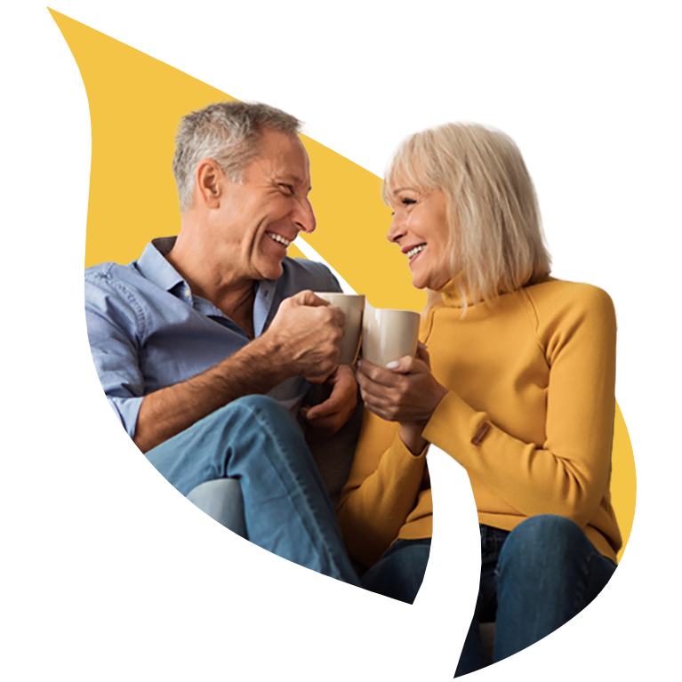 A senior couple looking at each other happily with mugs in their hands, over the Masonicare yellow leaf