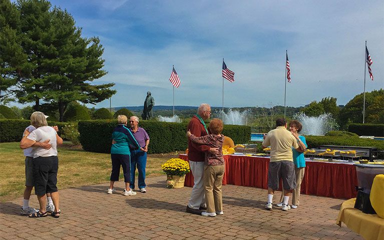Four senior couples dancing outside with American flags in the background. 