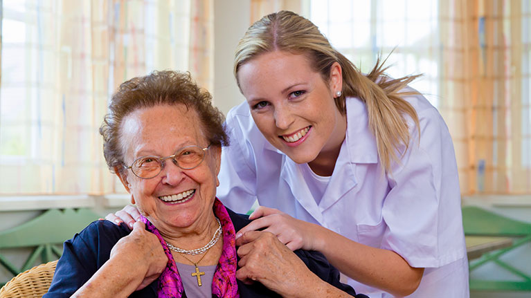 Female nurse smiling with her hands on a smiling senior patient's shoulders. 
