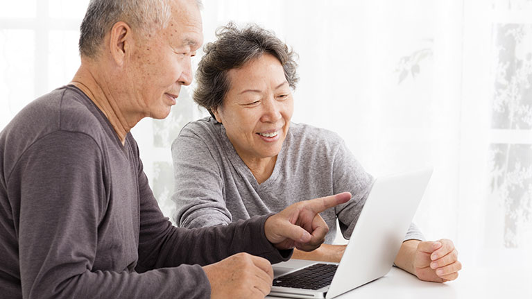 Senior couple smiling and pointing at laptop screen.