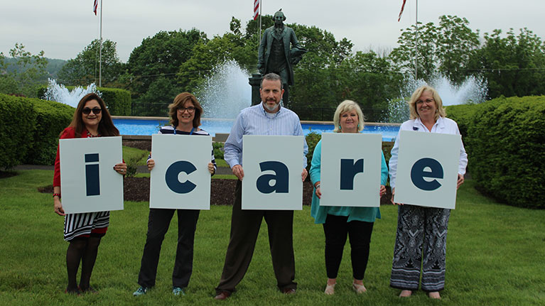Four women and one man outside holding signs that spell icare.