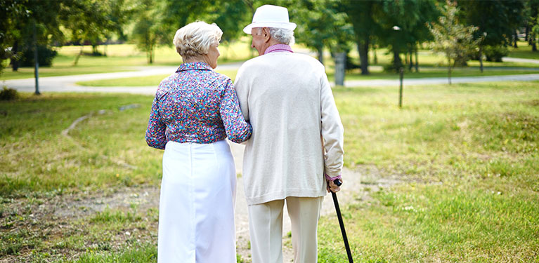 Older couple, dressed nicely walking on the grass with their backs towards us 