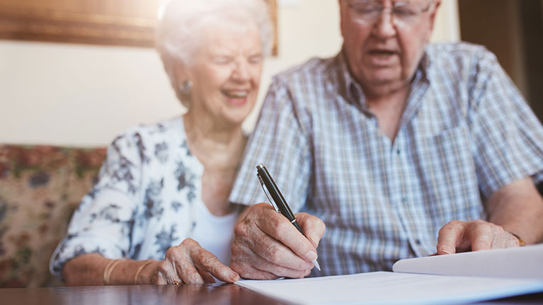 Senior couple smiling while signing papers.